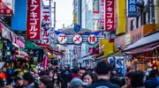 Crowds of people in a street, lined with shops, shop and cafe signs. 